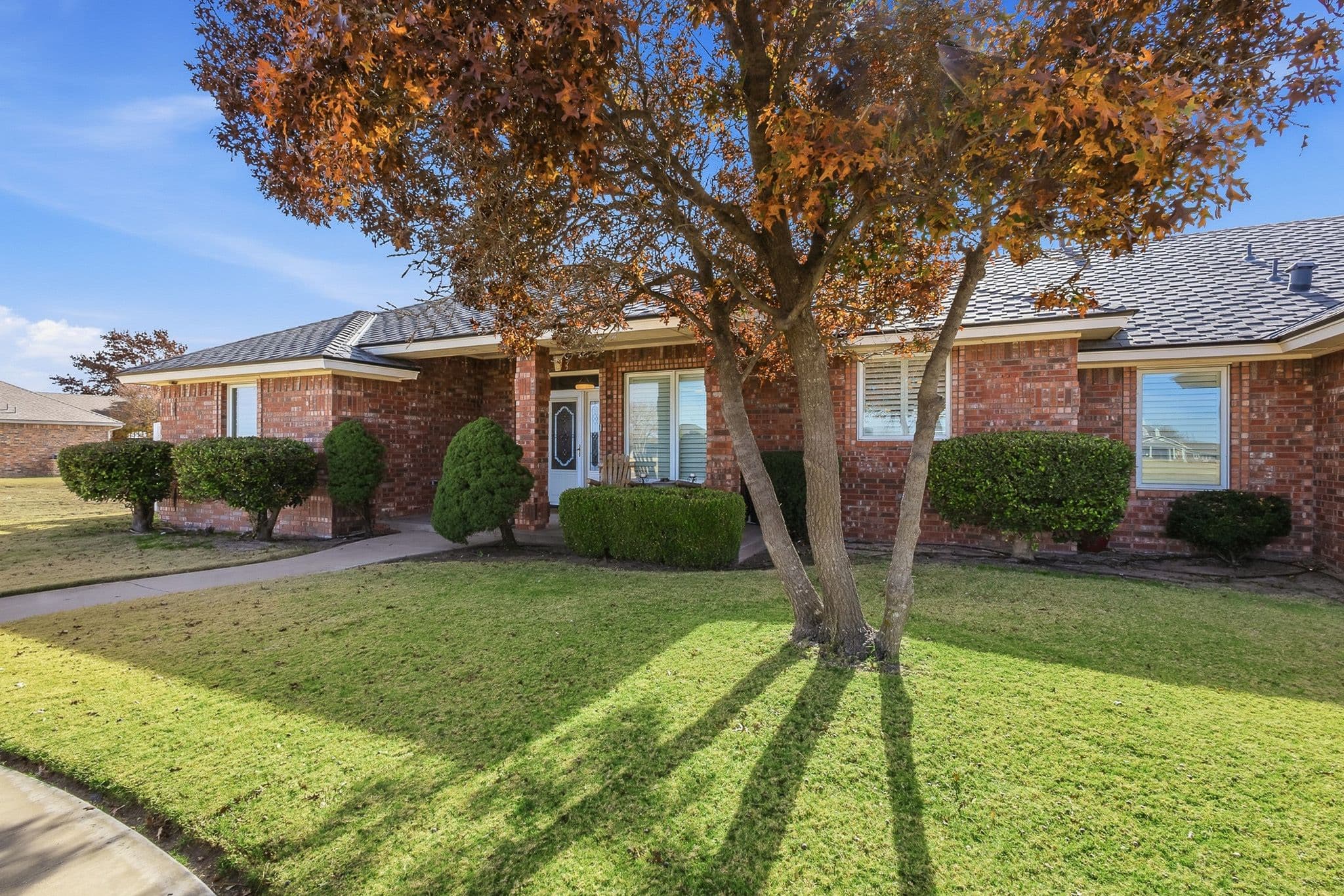 Low-profile brick ranch exterior in Muleshoe, TX framed by mature trees, shot in hand-blended HDR.
