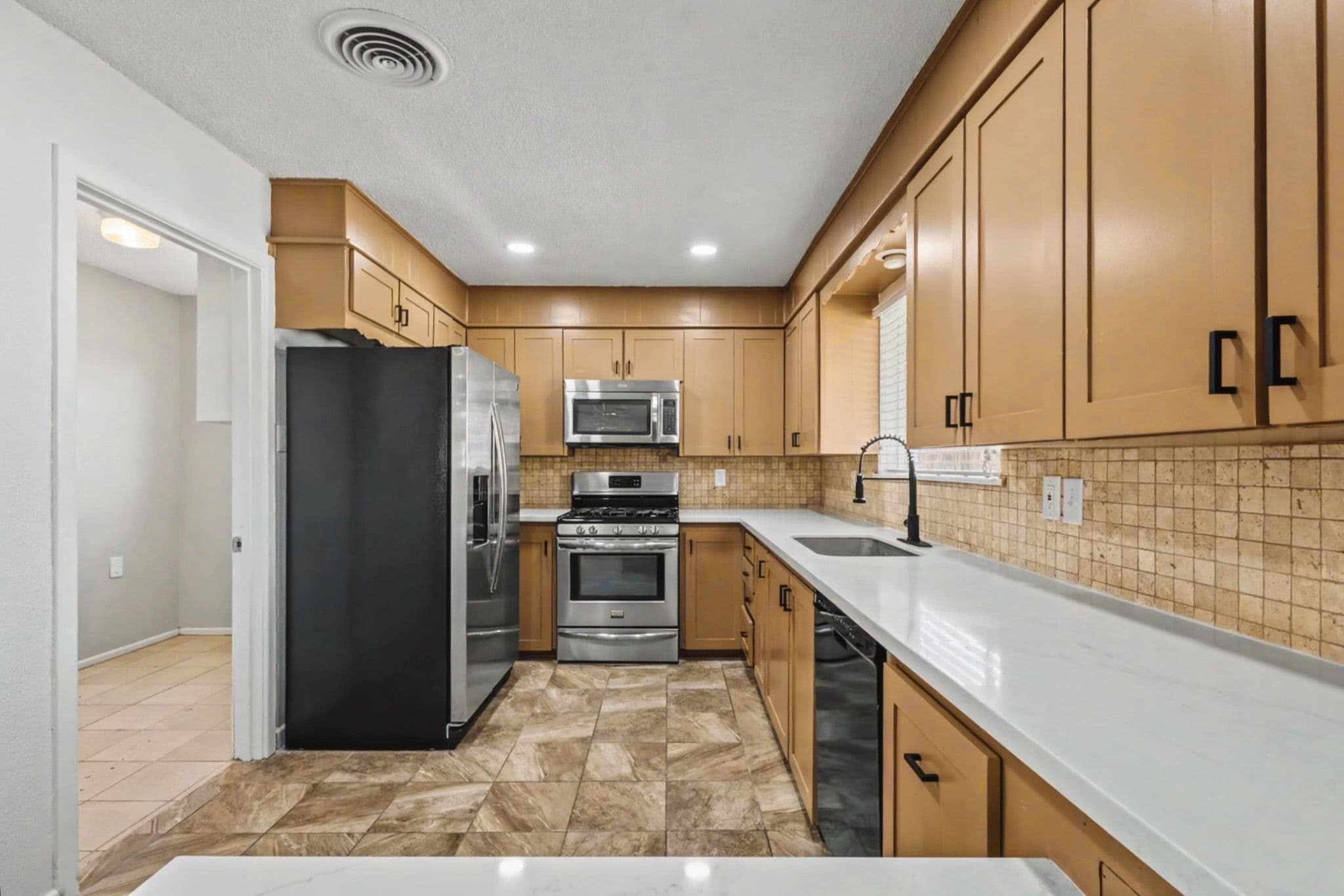 Kitchen opening into a dining area in a Levelland, TX ranch home with tile floors and neutral cabinetry.